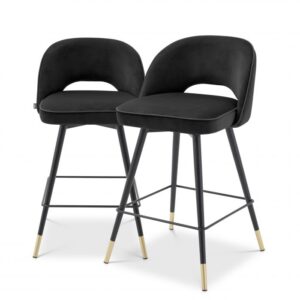Create a wow-worthy interior with the Cliff Counter Stool in Roche black velvet, that comes in a set of 2. Featuring black tapered legs with gold caps, the solid frame holds an armless back that is open at the bottom before the seat. Its stylish silhouette is accentuated with black faux leather piping.